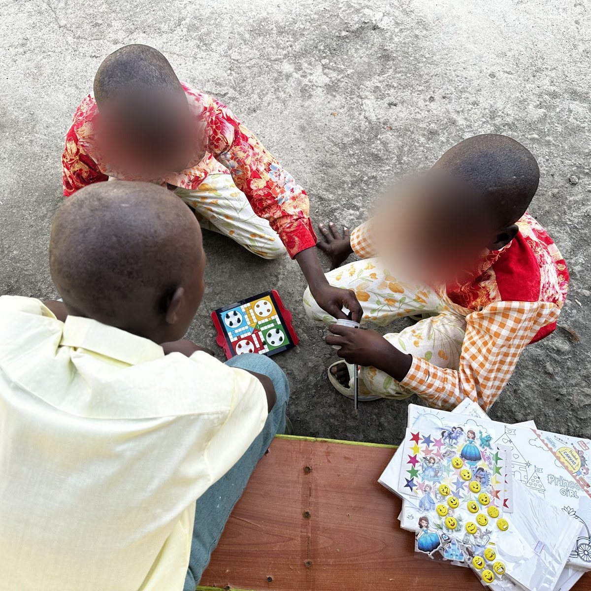 Children playing a board game beside art materials, faces blurred for privacy
